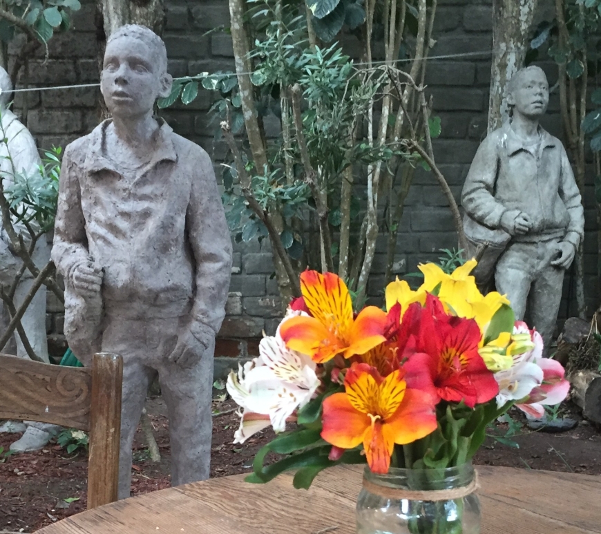 Wooden table with flowers in garden, Barranco, Lima, Peru with statues of children in the background